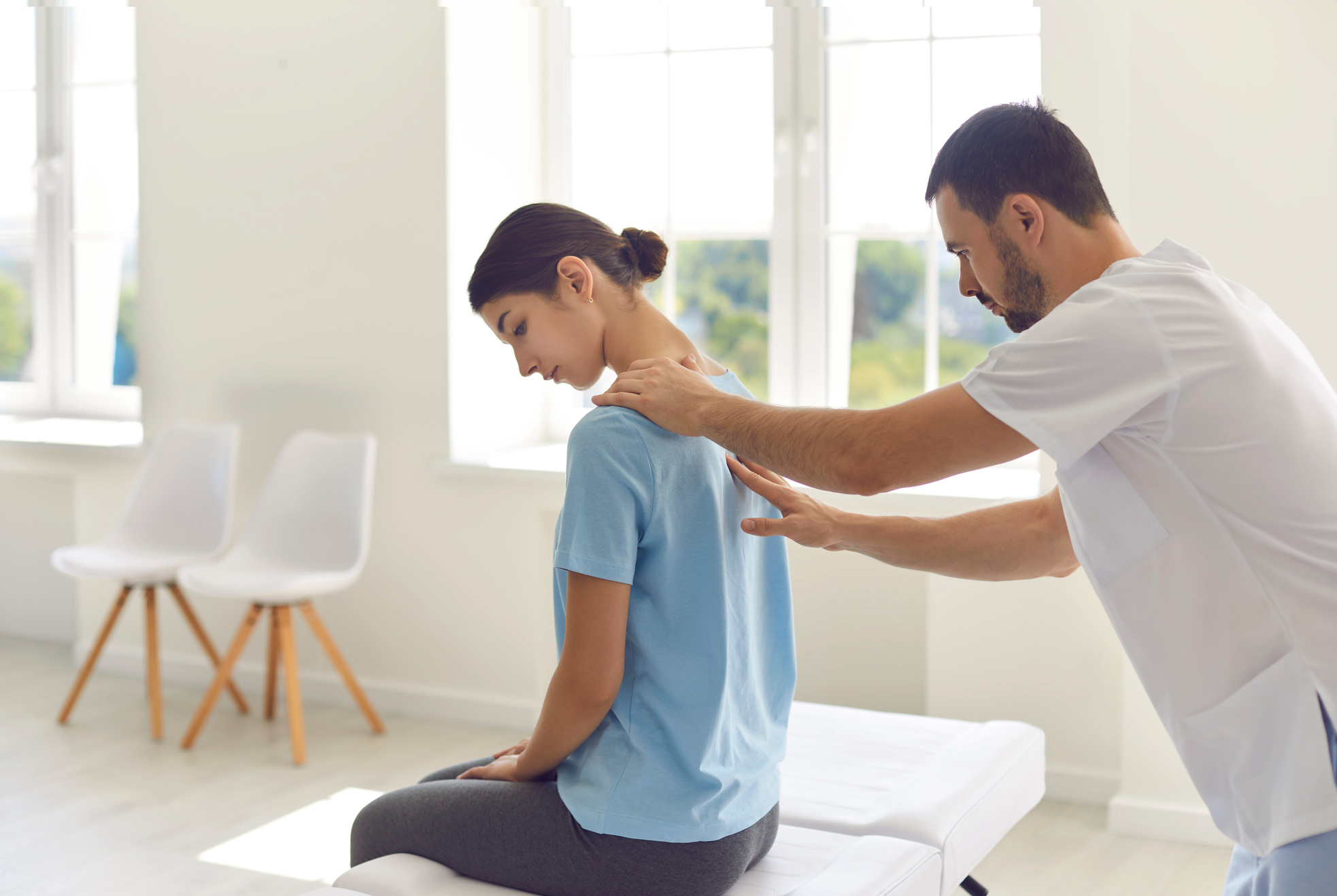 Licensed Doctor Helping Young Woman to Ease Back Pains in Modern Hospital Office